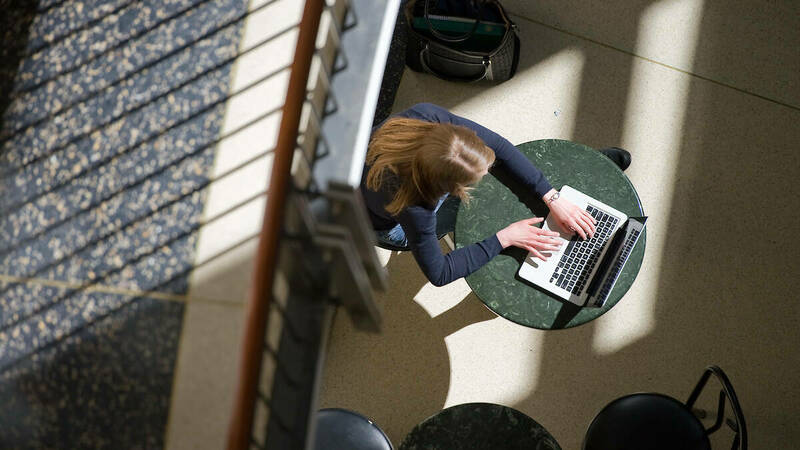 Overhead view of student working on laptop at round green table.